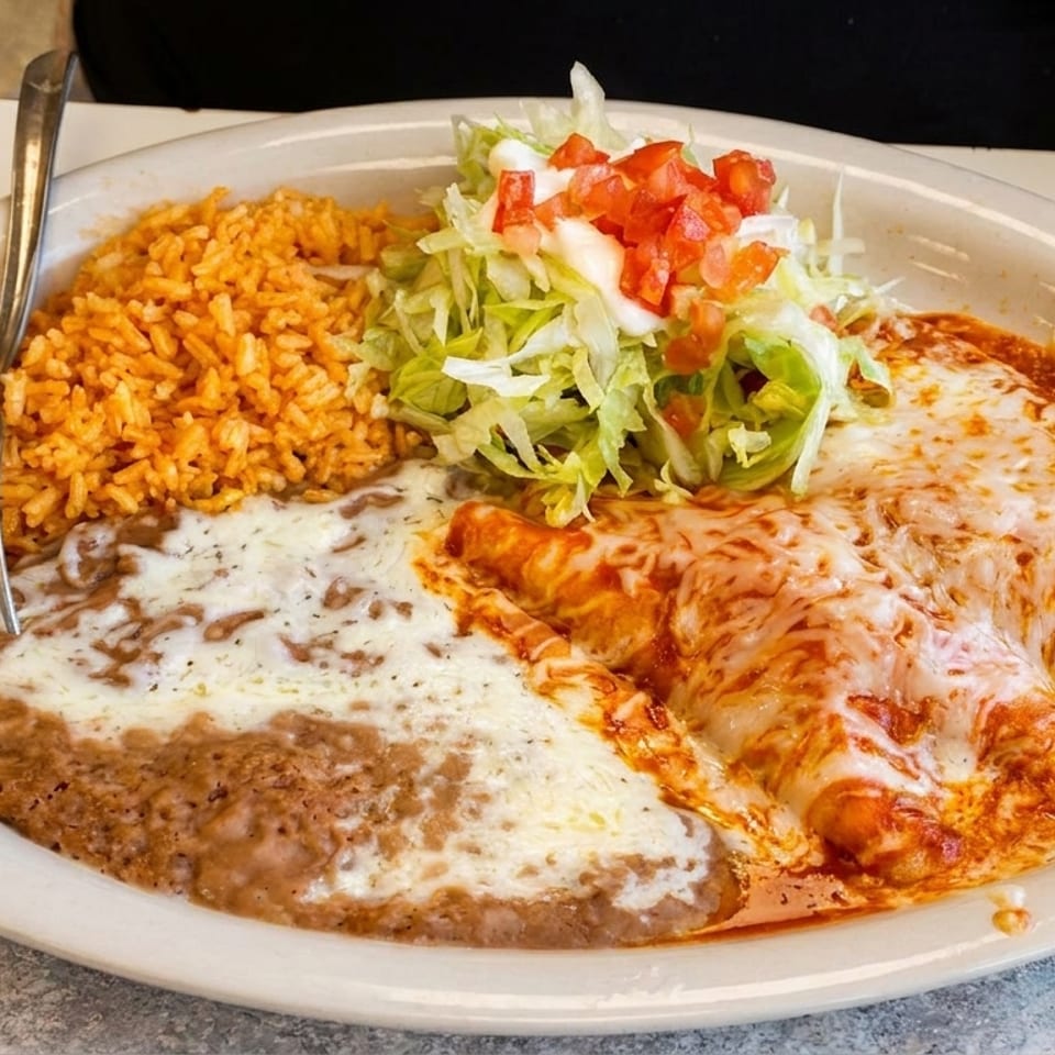 Cheesy enchiladas, refried beans, Spanish rice, and a fresh lettuce and tomato salad on a white plate.