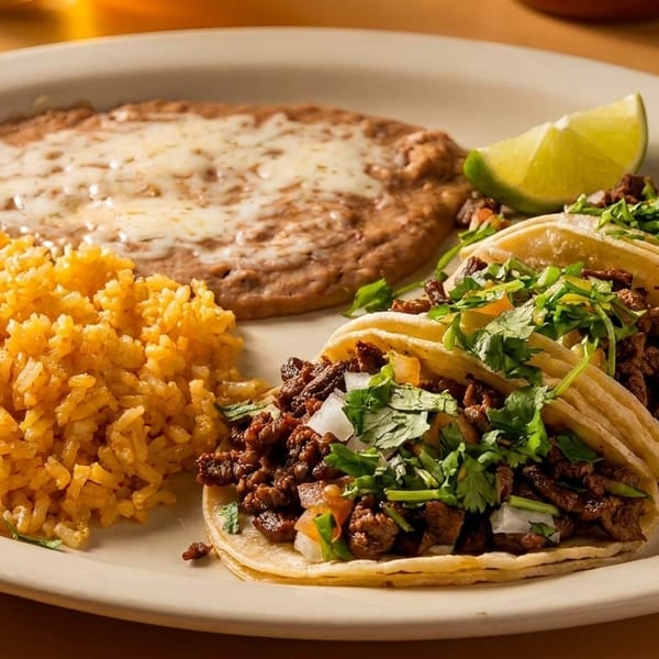 Plate of three carne asada tacos, yellow rice, and cheesy refried beans with a lime.
